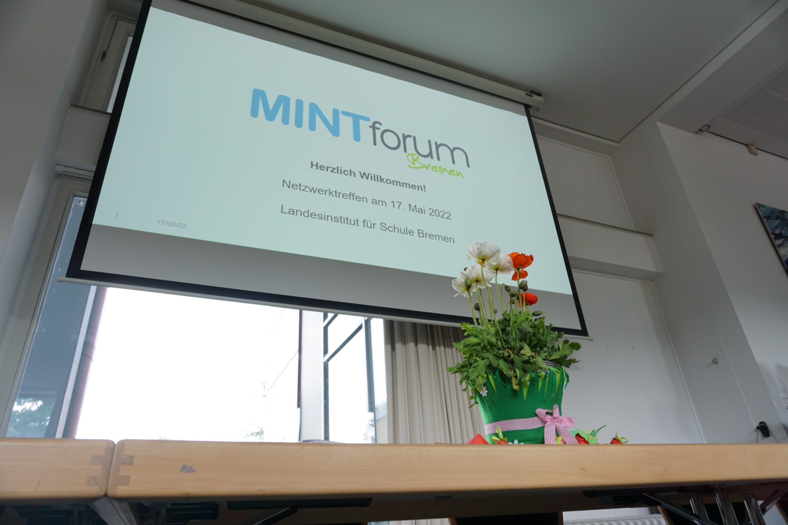 Eine Leinwand auf die eine Folie mit dem Titel MINTforum Bremen - Herzlich willkommen gestrahlt wird.